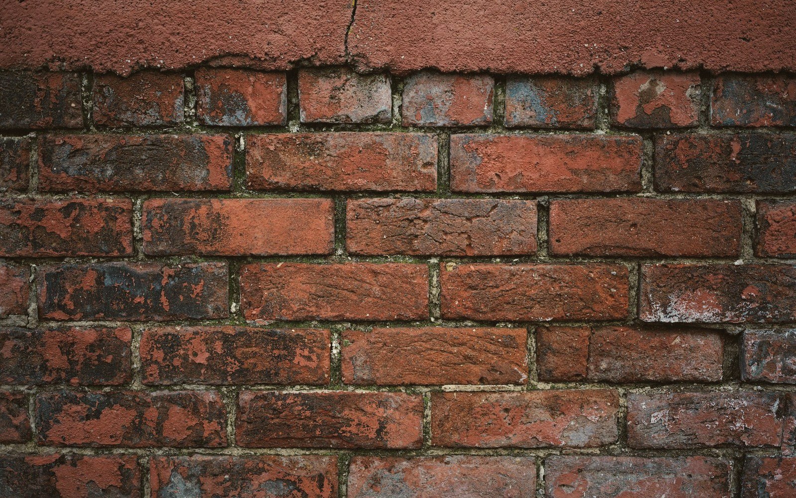 Weathered brick wall with cement render crumbling away at the top edge