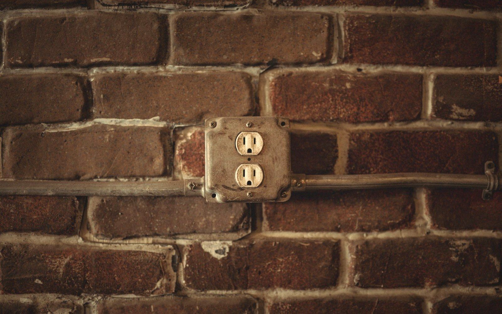 Electrical outlet mounted in a metal box with surface conduit on exposed brick