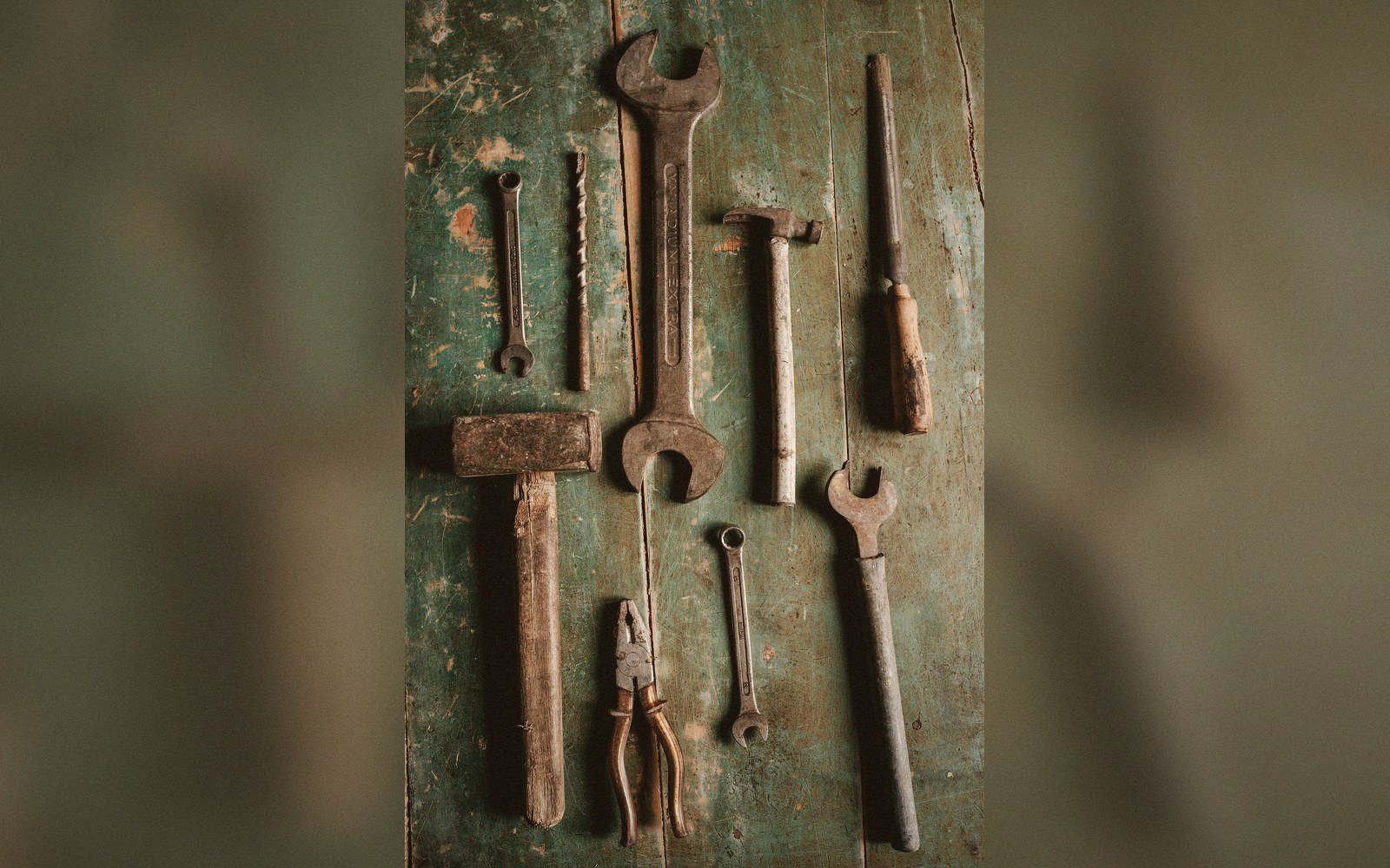 Rusty wrenches, pliers, a mallet and a screwdriver laid out on weathered green wood