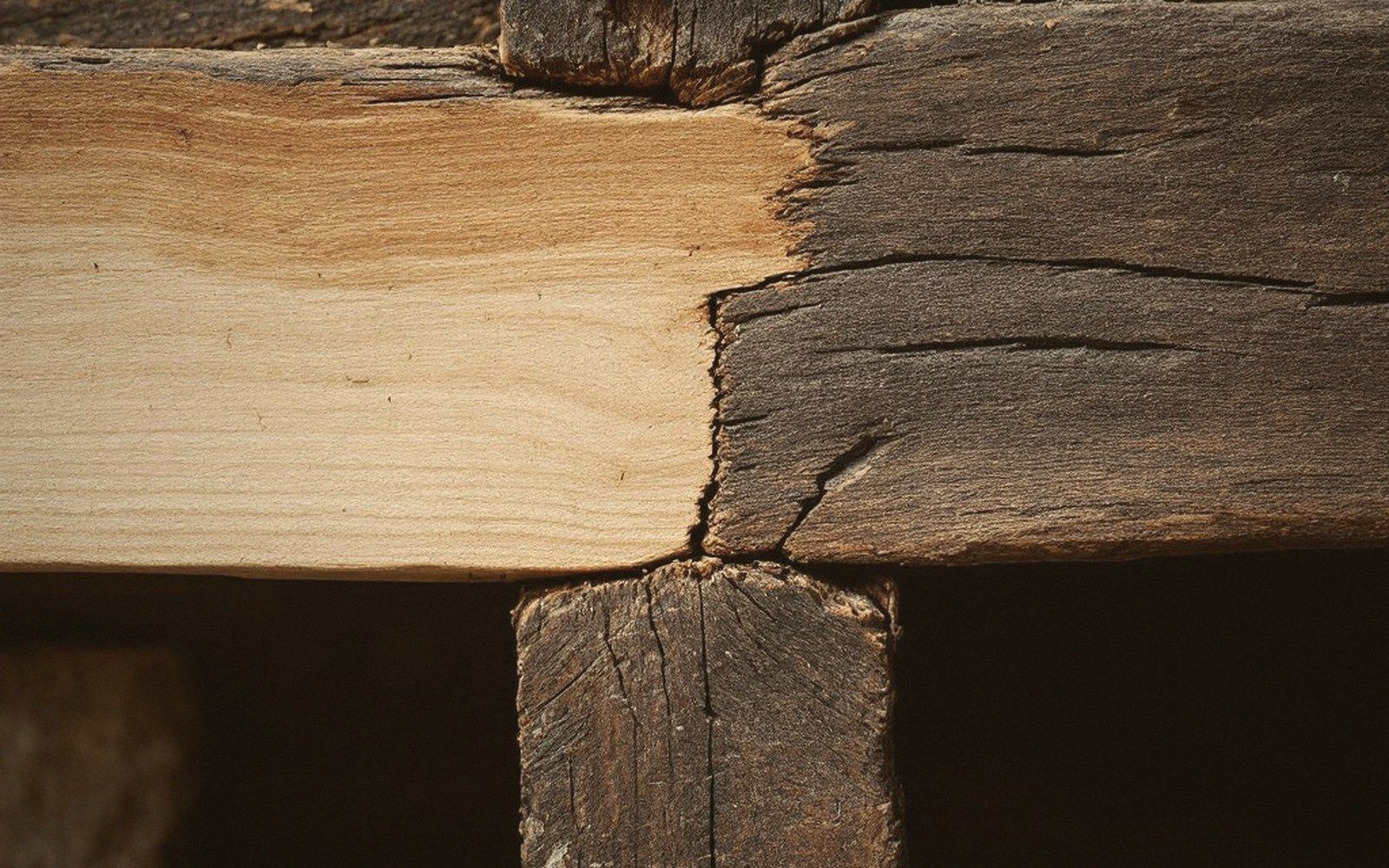 A pale new timber section joined to a weathered old beam at a scarf joint